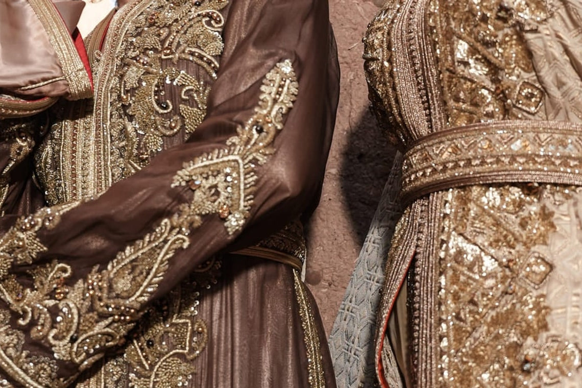 Alabaster Aria ivory Moroccan kaftan with gold embroidery and an ornate belt, beside a brown embroidered kaftan