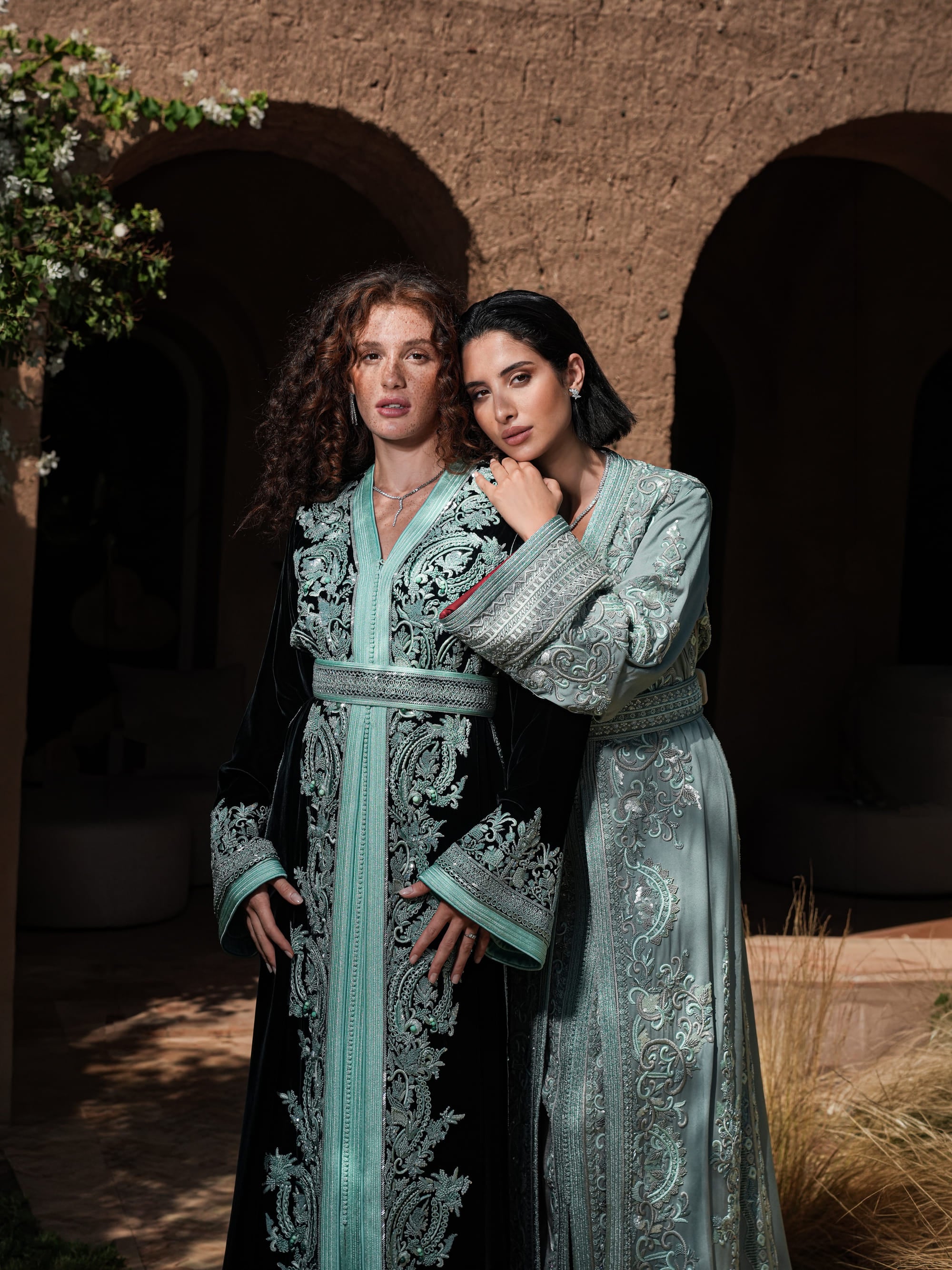 Cypress Portico deep green velvet Moroccan kaftan with sea-green embroidery, shown alongside a second look